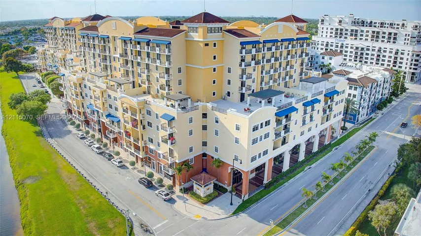 Multi-story residential complex featuring Mediterranean-inspired architectural details, barrel-tiled roofing, private balconies with blue awnings, and ground-level covered loggias
