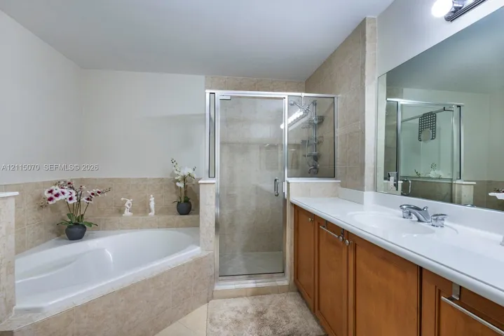 Bathroom featuring a corner soaking tub with tile surround, a glass-enclosed shower, wood-finish cabinetry, a white countertop with integrated sink, and an expansive wall-mounted mirror