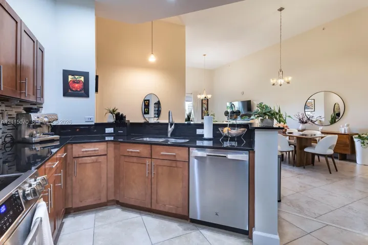 Kitchen featuring flat-panel wood cabinetry, dark stone countertops, stainless steel appliances, tile flooring, and vaulted ceilings