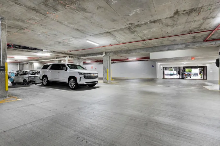 Covered parking garage featuring smooth concrete flooring, exposed structural concrete ceilings, industrial-style lighting, and steel support pillars