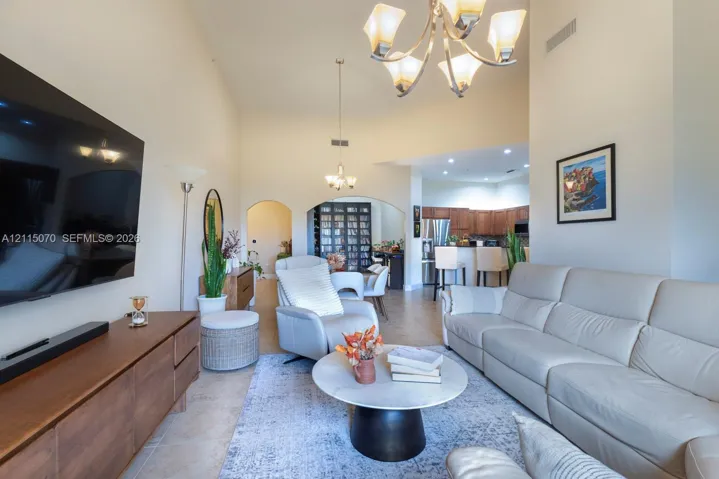 Vaulted ceilings with multi-tier chandelier lighting, arched wall openings, and tile flooring