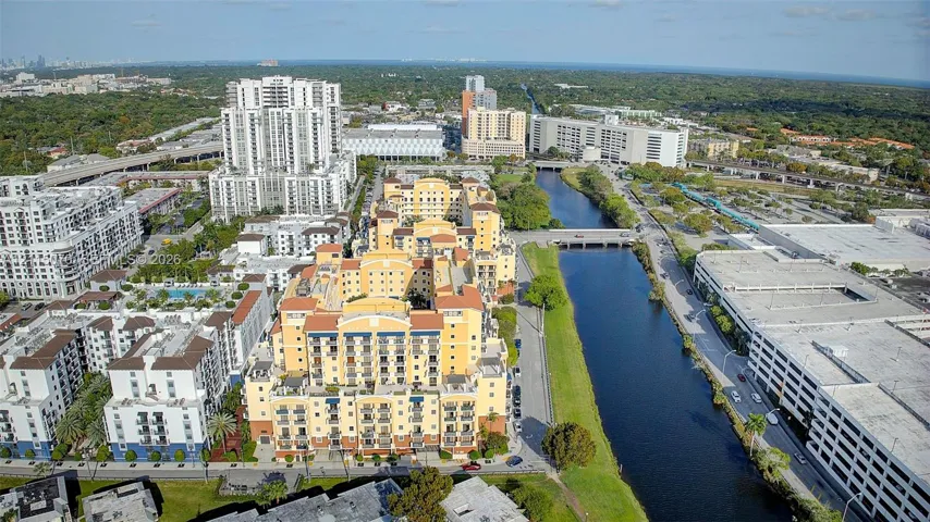 Aerial view of a multi-story residential complex featuring Mediterranean-inspired architecture, terracotta-toned exterior finishes, multiple balconies, a tiled roofline, and proximity to an adjacent waterway