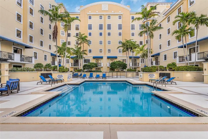 In-ground swimming pool featuring a tiled waterline, metal handrails, and a wide paver surround with integrated landscaping including mature palm trees