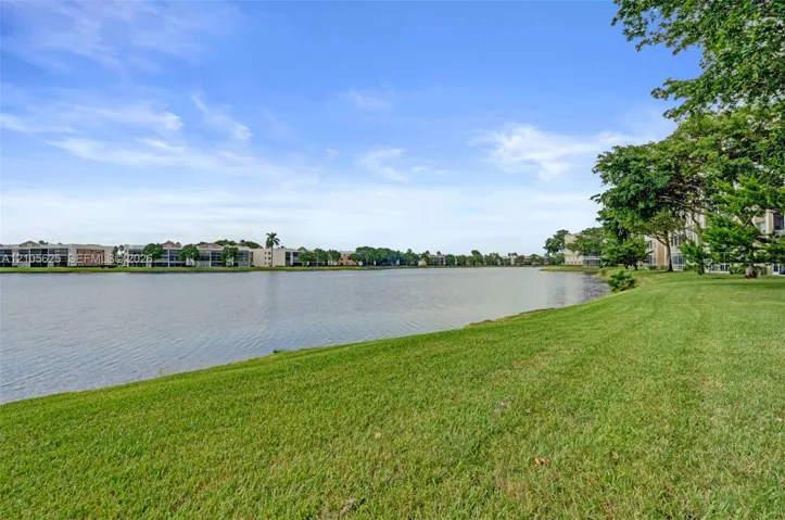 Waterfront grounds featuring a maintained lawn, mature trees, and a lake