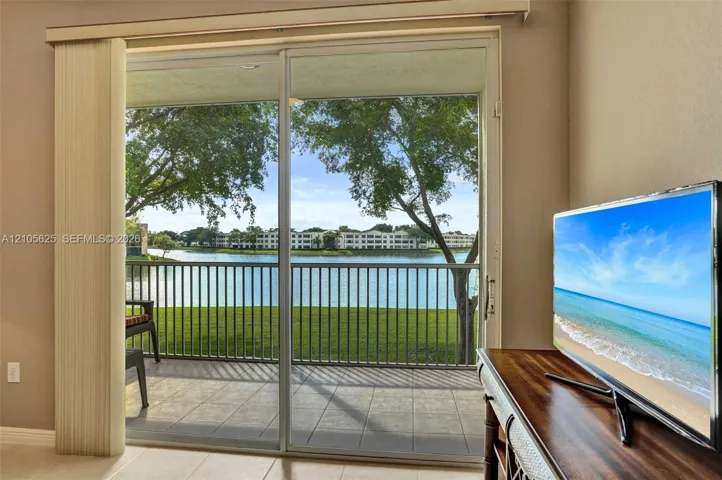 Sliding glass door opening to a tiled balcony with a metal railing, overlooking a water feature and mature trees