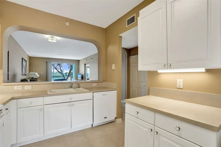 Kitchen featuring white cabinetry, solid surface countertops, integrated dishwasher, and a pass-through opening