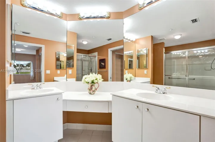 Dual-sink vanity with white cabinetry, solid surface countertops, expansive wall-to-wall mirrors, and overhead lighting fixtures