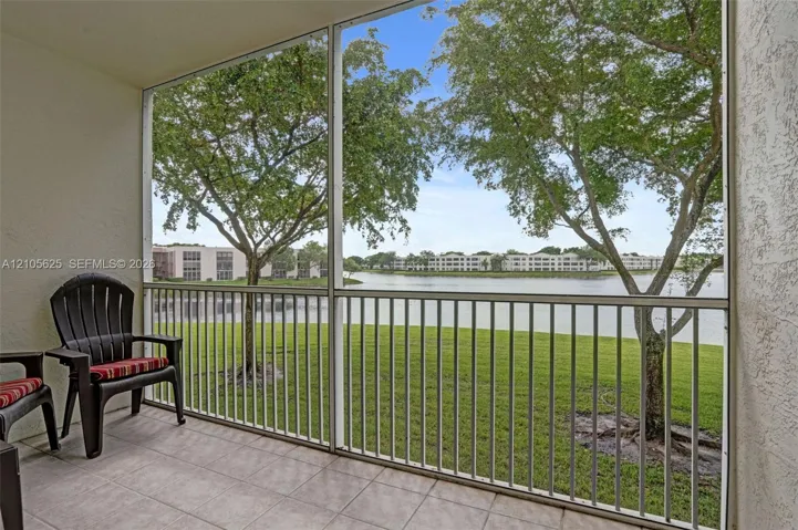 Screen-enclosed patio featuring a tiled floor and metal railing, overlooking a lake and mature trees