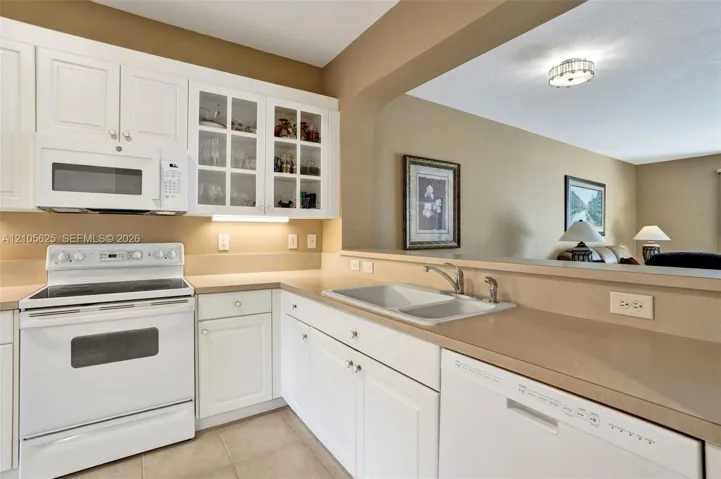 Kitchen featuring white shaker-style cabinetry, glass-front upper cabinet doors, solid-surface countertops, dual-basin sink with metallic faucet, and built-in appliances