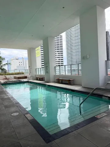 Covered outdoor swimming pool featuring large-format tile decking, recessed ceiling lighting, glass panel perimeter railing, and integrated stairs