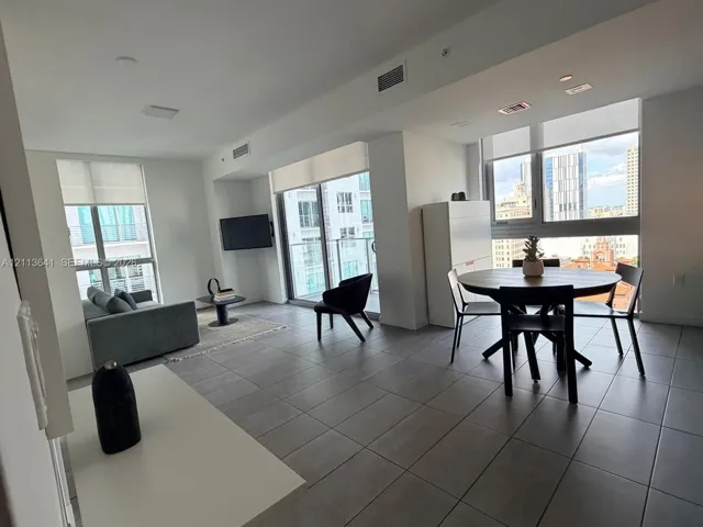 Open-concept interior featuring large-format tile flooring, expansive floor-to-ceiling windows, and sliding glass doors with access to a private balcony