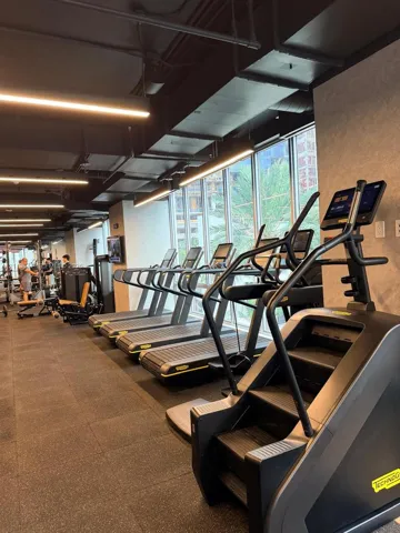 Fitness area featuring floor-to-ceiling windows, high-contrast industrial-style exposed ceilings, linear LED lighting, and resilient rubber flooring