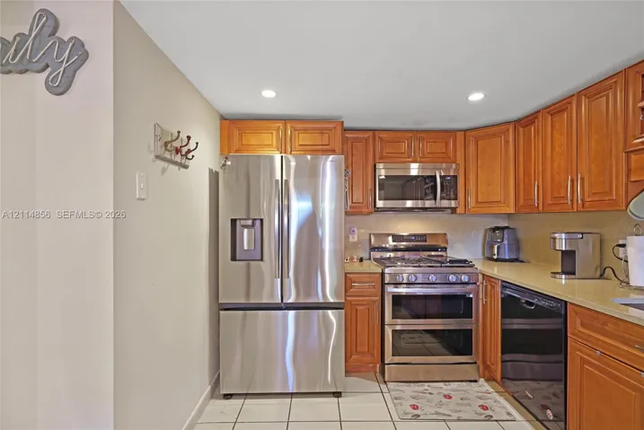 Kitchen featuring natural wood cabinetry, stainless steel appliances, solid surface countertops, recessed lighting, and tile flooring