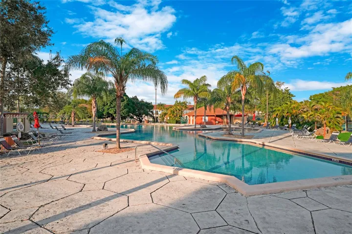 Swimming pool with integrated steps, surrounded by stone-finish deck pavers and mature palm trees