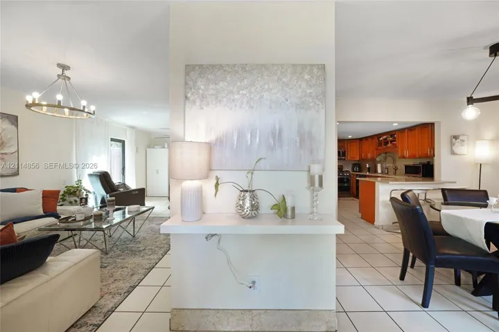 Open-concept interior featuring large-format tile flooring, central partition wall with built-in display shelf, and chandelier lighting