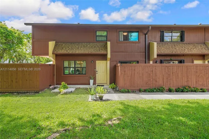 Two-story exterior featuring wood-paneled siding, shingle-style roof accents, horizontal wood privacy fencing, and multi-pane windows