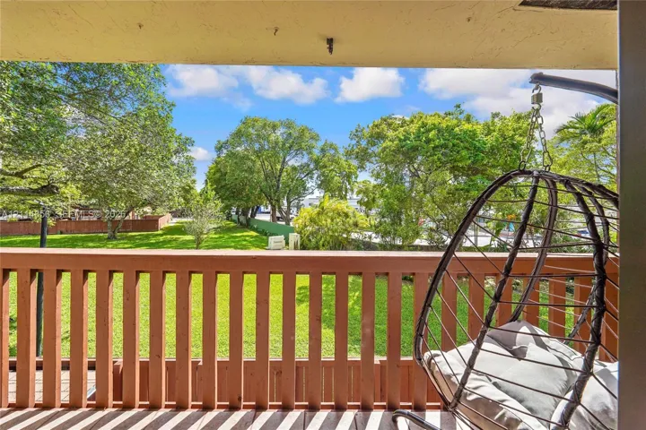 Covered balcony featuring a wood-style railing and an outdoor space overlooking a landscaped yard with mature trees