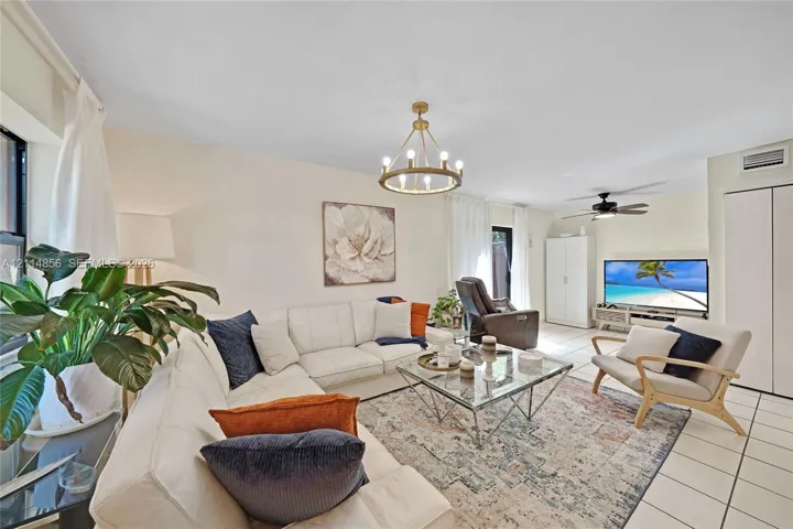 Neutral-toned interior space featuring light-colored tile flooring, a circular chandelier with brass finish, and a ceiling-mounted fan with light fixture