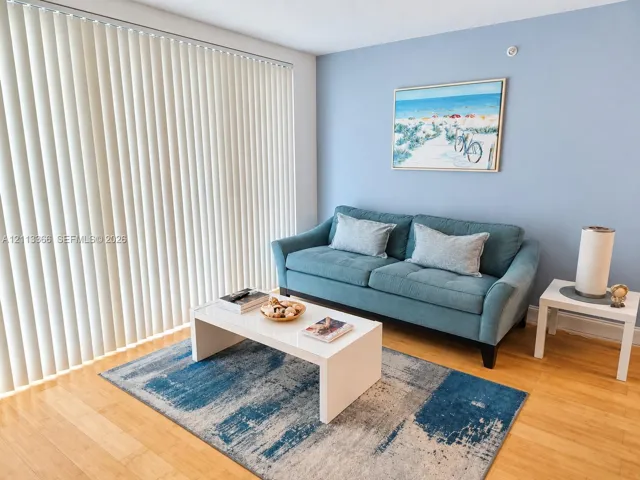 Living area featuring wood-finish flooring, light blue painted walls, and vertical blinds