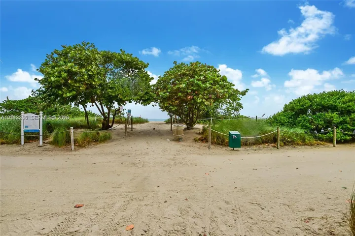 Sandy beach access featuring rope-post fencing, mature coastal trees, and native vegetation