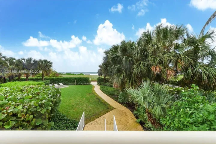 Expansive grounds featuring a manicured lawn, paver walkway, mature palm trees, and dense perimeter landscaping