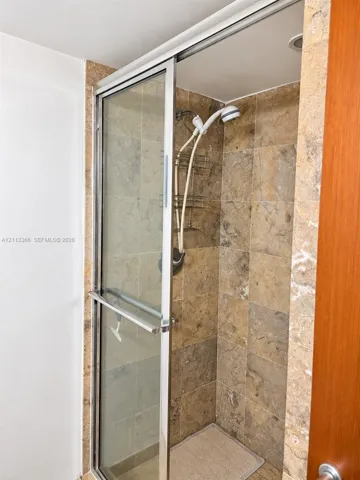 Shower enclosure featuring natural stone wall tile, glass sliding door with chrome frame, and a hand-held shower fixture