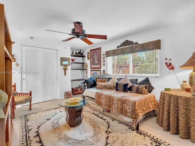 Room featuring light-toned flooring, louvered closet doors, built-in shelving, a ceiling fan, and window blinds