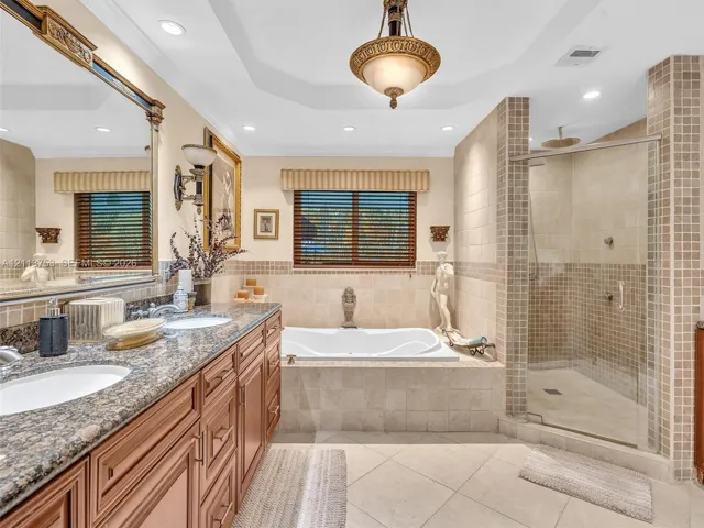 Bathroom featuring a dual-sink vanity with stone countertops, a deep soaking tub, a walk-in glass-enclosed shower with tiled surround, and decorative pendant lighting