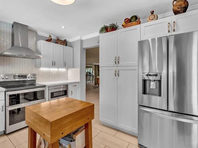 Kitchen featuring white shaker-style cabinetry, stainless steel appliances, a herringbone-pattern tile backsplash, and ceramic tile flooring