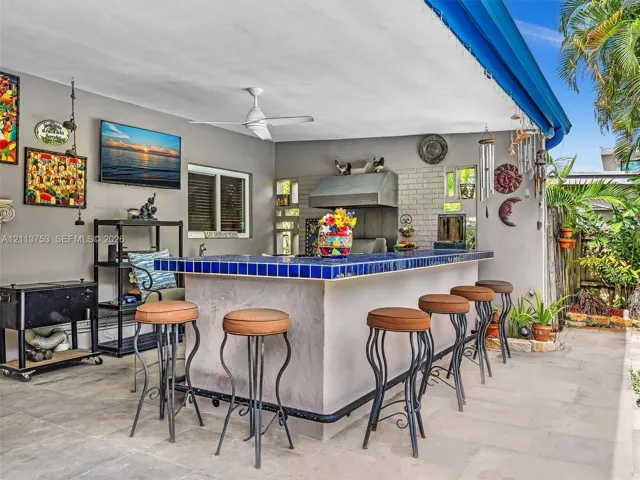 Covered outdoor patio featuring a built-in bar with blue tile countertop, stainless steel ventilation hood, and stone-finish flooring