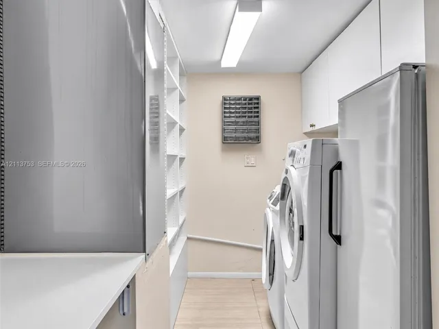 Utility area featuring floor-to-ceiling built-in shelving, white overhead cabinetry, and wood-finish flooring