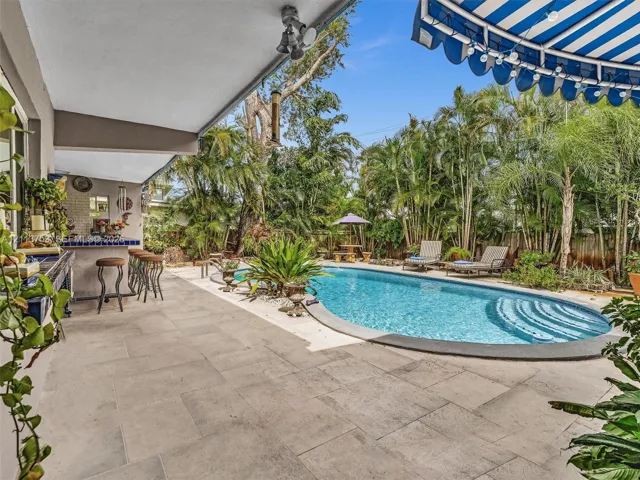 Covered patio with large-format stone pavers, built-in tiled wet bar, and kidney-shaped swimming pool with concrete surround