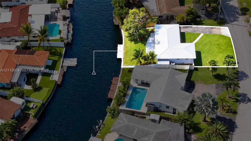 Waterfront property featuring a private dock, expansive lawn, paved driveway, and mature landscaping