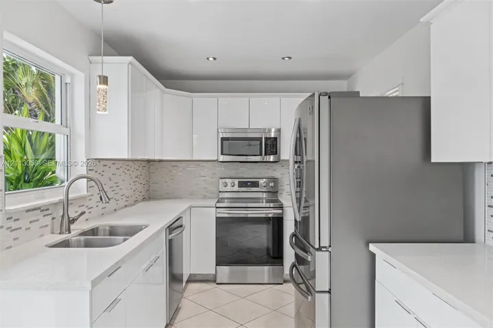 Kitchen featuring white gloss cabinetry, quartz countertops, stainless steel appliances, a mosaic tile backsplash, and ceramic tile flooring