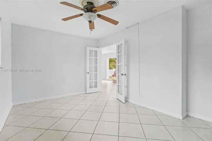 Interior space featuring large-format diagonal tile flooring, white French doors with glass panes, and a ceiling-mounted fan with wood-finish blades