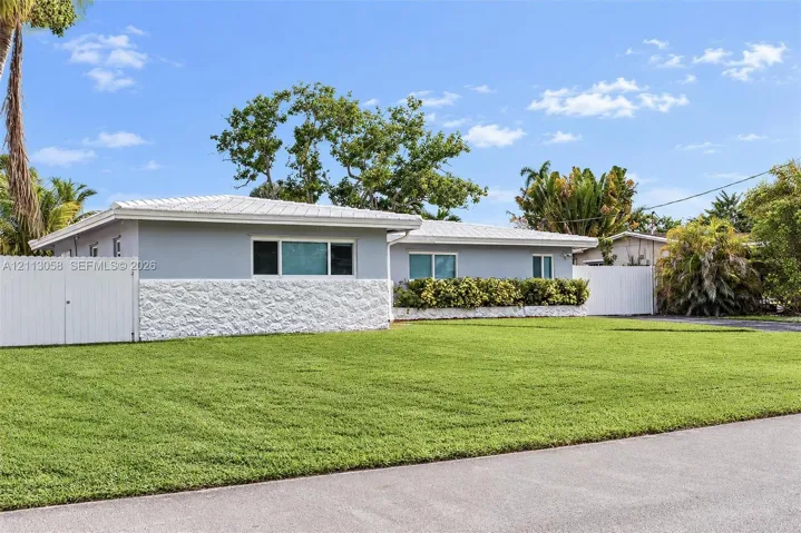 Single-story residence featuring a textured masonry facade, light-toned exterior finish, metal roofing, and privacy fencing enclosing the perimeter