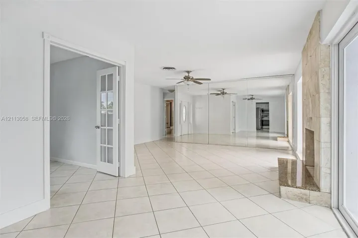 Neutral-toned tile flooring, floor-to-ceiling mirrored wall paneling, fireplace featuring a stone-tile hearth, and glass-paned French doors