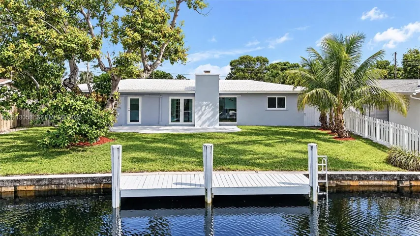 Waterfront property featuring a private dock, expansive lawn, exterior chimney, and white picket fencing