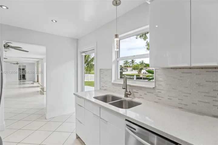 Kitchen featuring high-gloss white cabinetry, quartz countertops, a stone-pattern tile backsplash, stainless steel dual-basin sink with a pull-down faucet, and recessed lighting
