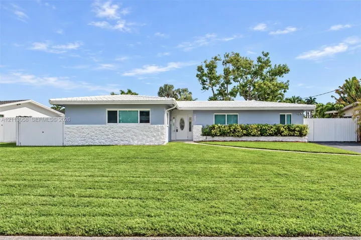 Single-story exterior featuring light-toned masonry, textured stone wainscoting, a covered entry with an oval-glass door, and vinyl perimeter fencing