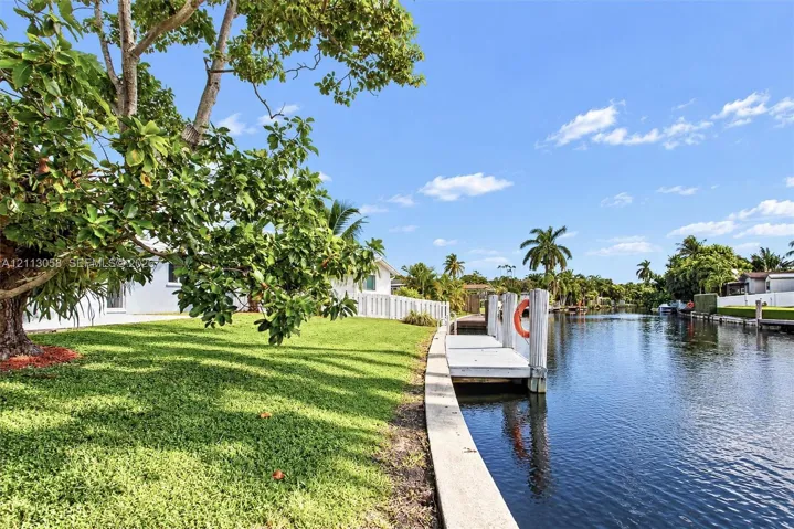 Canal-front property featuring a private dock, concrete seawall, mature landscaping, and an expansive lawn