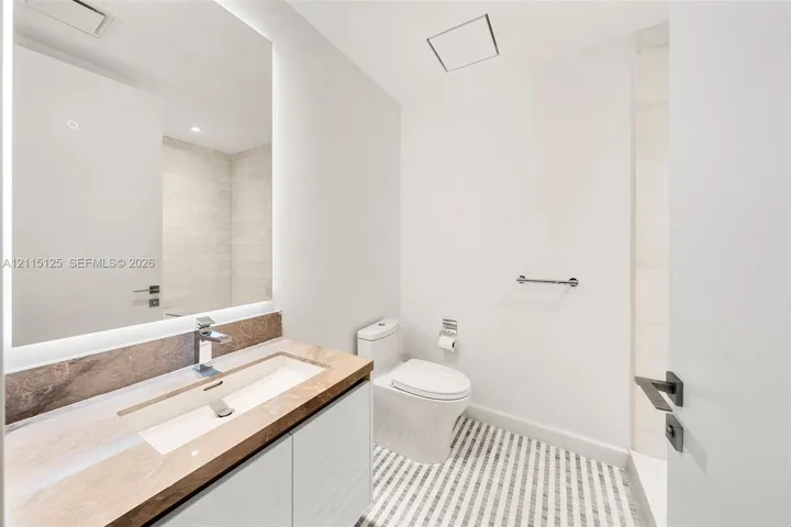 Floating vanity with stone-finish countertop, integrated sink, backlit mirror, and patterned tile​​‌​​​​‌​​‌‌​‌‌​​​‌‌​‌​‌​‌​​​‌​​ flooring