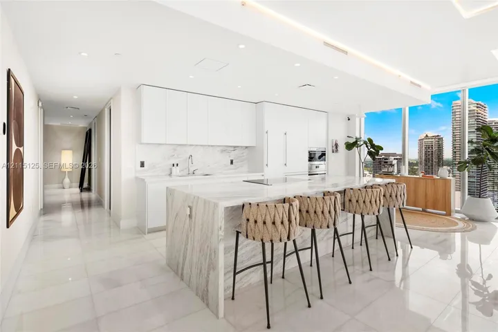 Kitchen featuring a waterfall-edge stone island, stone backsplash, flat-panel cabinetry, built-in appliances, and polished stone flooring