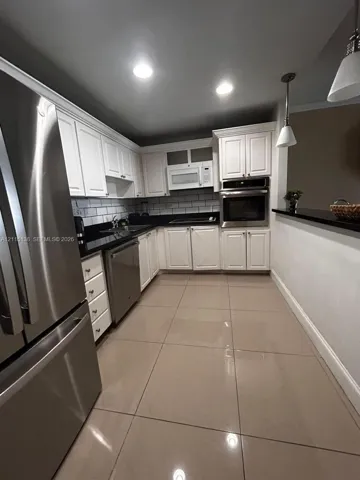 Kitchen featuring white shaker-style cabinetry, dark stone countertops, subway tile backsplash, stainless steel appliances including a built-in wall oven, and large-format tile flooring