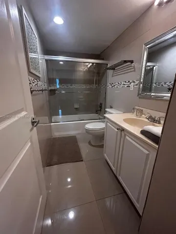 Full bathroom featuring a vanity with integrated sink, glass-enclosed shower and tub combination, neutral large-format floor tiling, and a mosaic tile backsplash