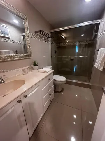 Bathroom featuring white cabinetry, integrated countertop with oval sink, glass-enclosed shower, mosaic tile accent border, and large-format tile flooring