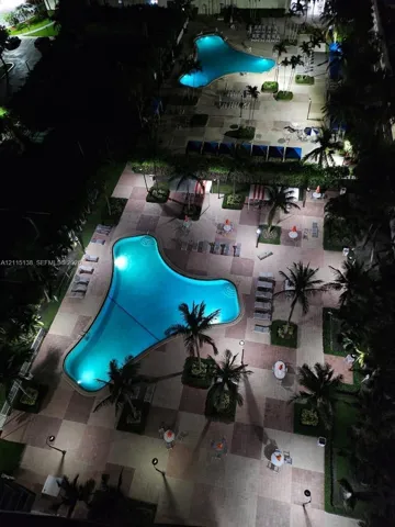 Dual swimming pools featuring tiled decking, paved walkways, palm tree landscaping, and overhead lighting