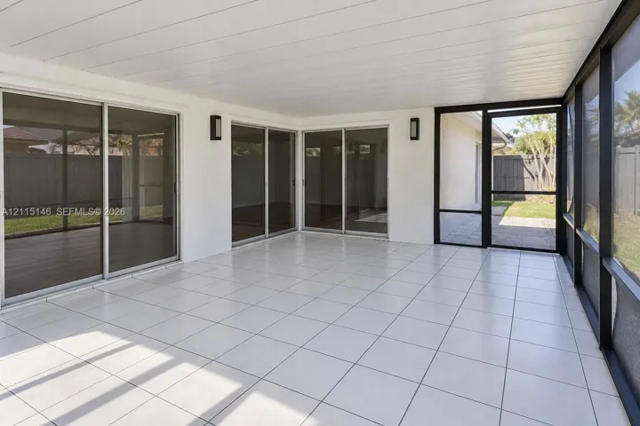Screened-in patio featuring tile flooring, a paneled ceiling, dual wall-mounted light fixtures, and multiple sliding glass doors