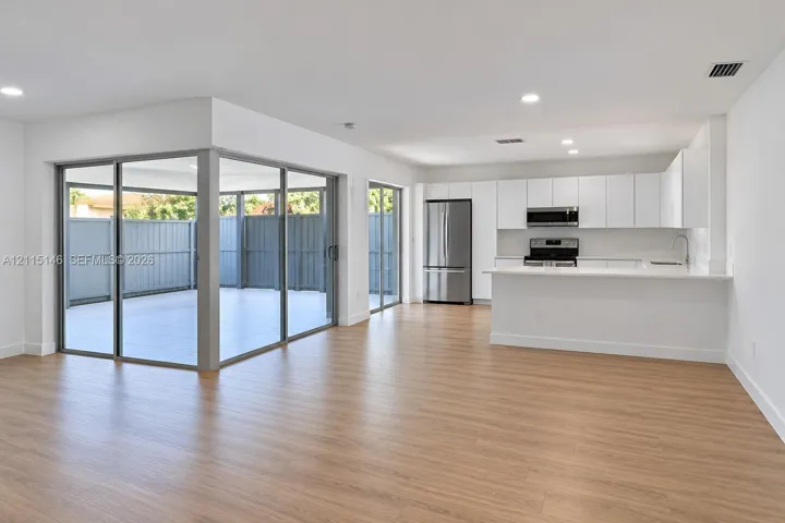 Open-concept interior featuring wood-finish flooring, white cabinetry, a kitchen island with a solid-surface countertop, stainless steel appliances, and large sliding glass doors