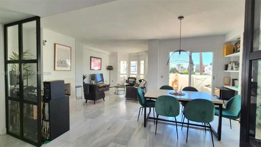 Open-concept interior featuring light stone flooring, a floor-to-ceiling black metal-framed glass partition, a built-in fireplace, recessed shelving, and a sliding glass door